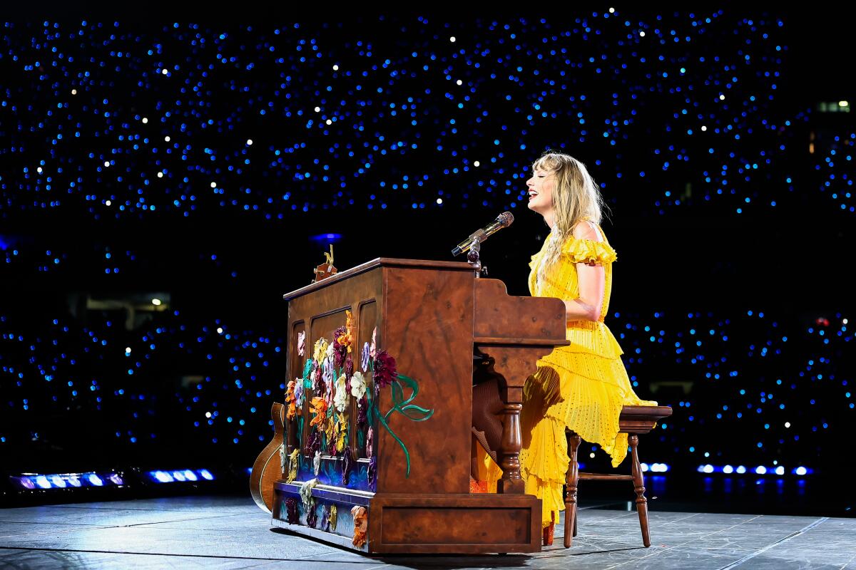 Taylor Swift performs onstage behind a piano.