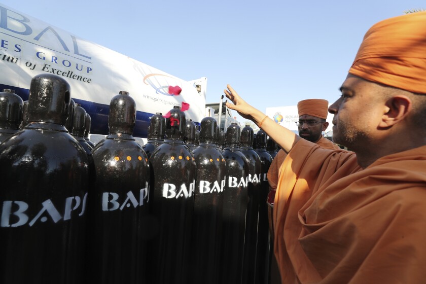 Brahmavihari Swami, the head of BAPS Shri Swaminarayan Mandir, the main Hindu temple in Abu Dhabi, throws rose petals during a blessing ceremony before shipping hundreds of liquid oxygen cylinders and massive containers of compressed oxygen to India, in Jebel Ali Free Zone, Dubai, United Arab Emirates, Monday, May 10, 2021. The organizers, Indian owners of Global Gases Group, a Dubai helium factory, shifted production to oxygen when the latest surge in virus cases hit India. (AP Photo/Kamran Jebreili)