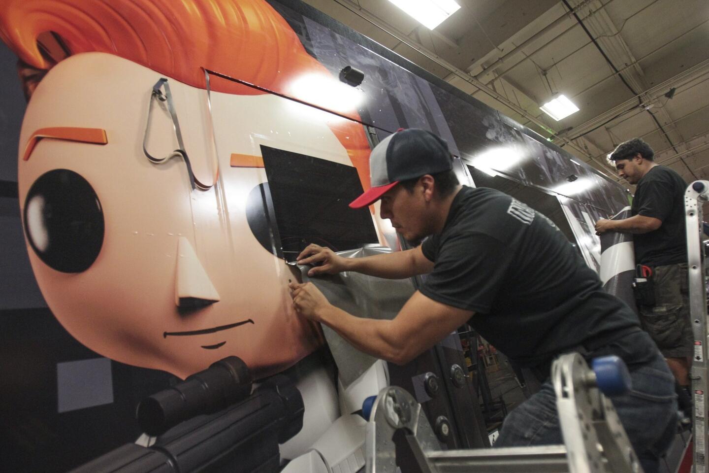 Oscar Santos, left, and David Garcia work on a section of transit vinyl as they and a crew put on an advertising wrap for TBS television host Conan O'Brien's talk show on a trolley car.