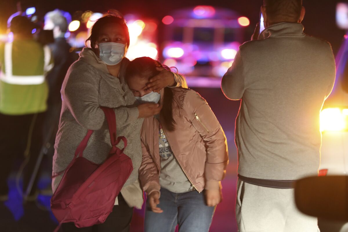 A woman embraces a young girl as they walk away from a crash scene