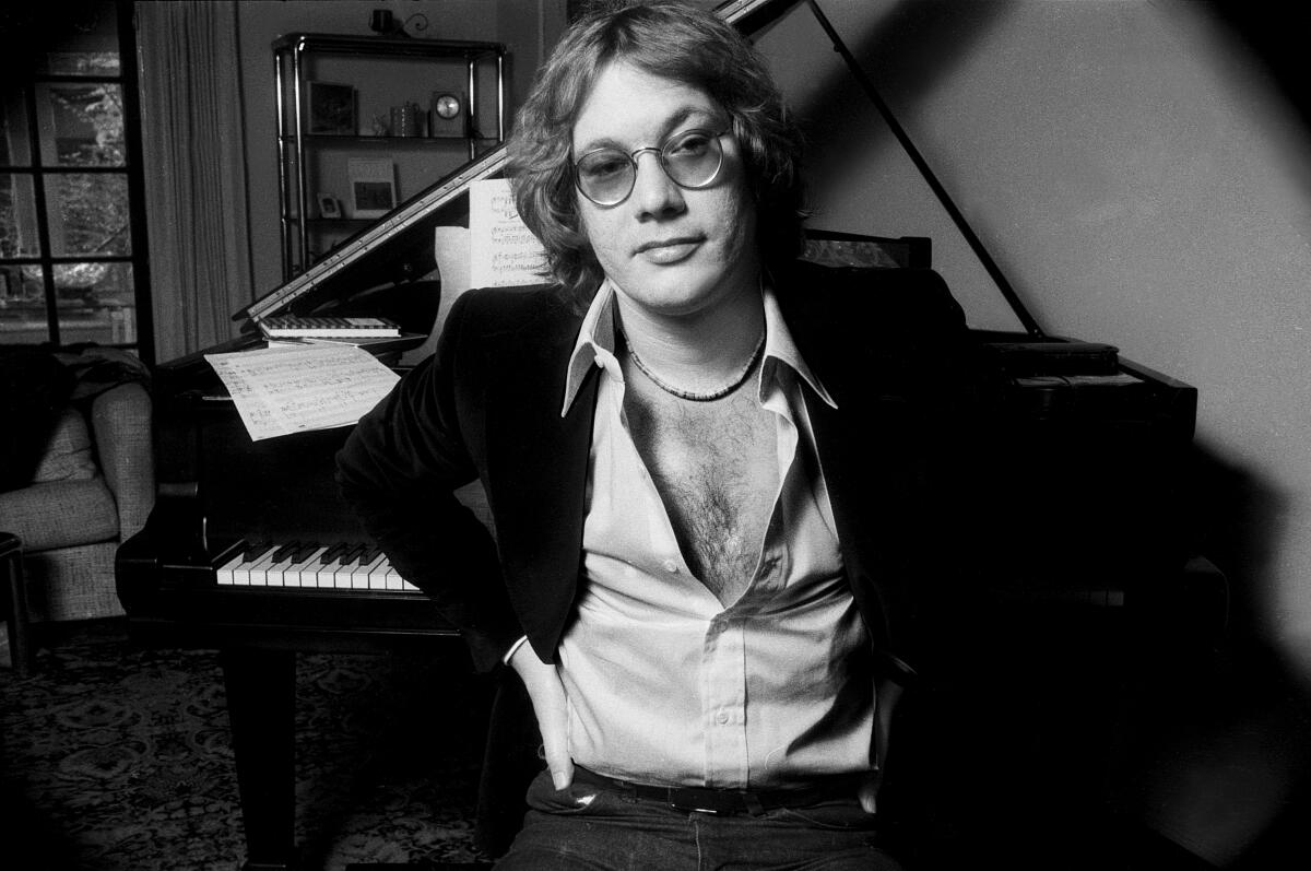 A musician poses for a portrait in front of a piano