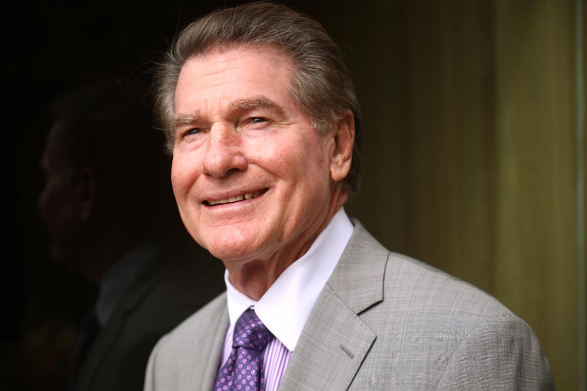 Steve Garvey smiles while wearing a gray suit and purple patterned tie.