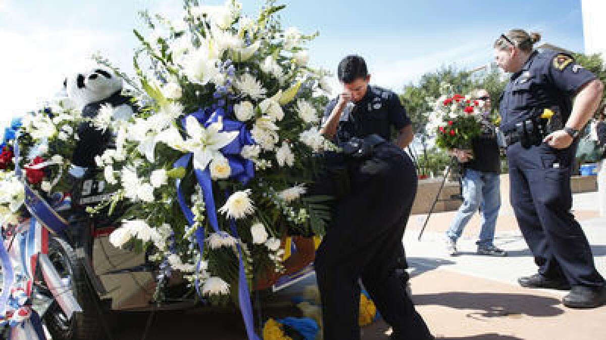 A Dallas police officer wipes away a tear as other officers adjust flowers on a police cruiser.