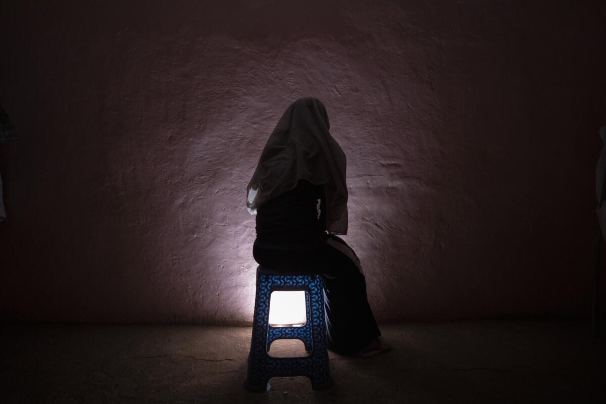 A person sits with their back to the camera in a dark room with a light at their feet..