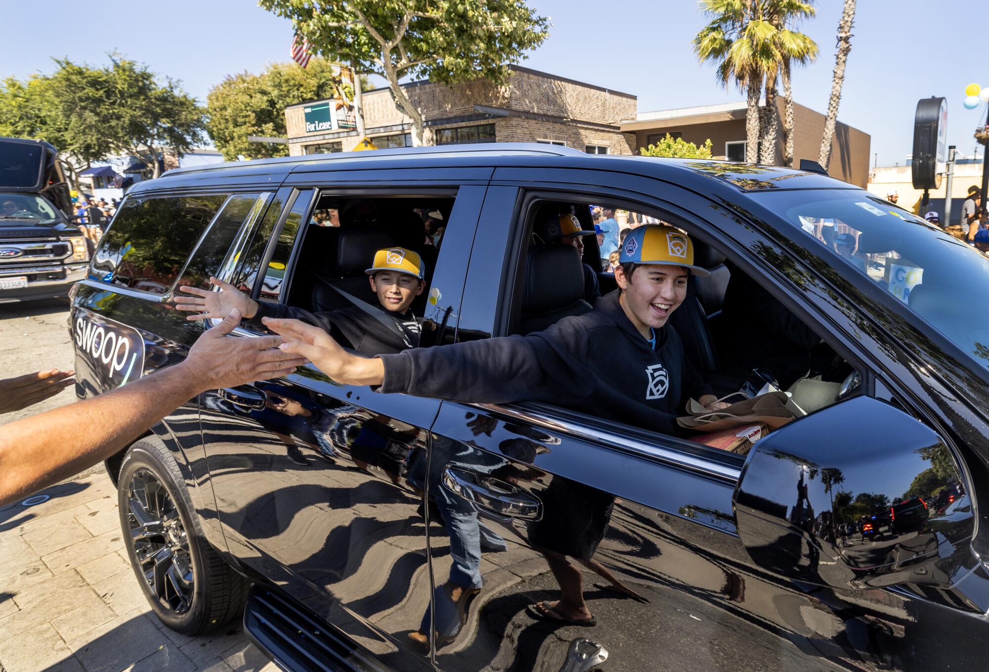 A boy in a baseball cap gives a passerby a high-five from a car window.