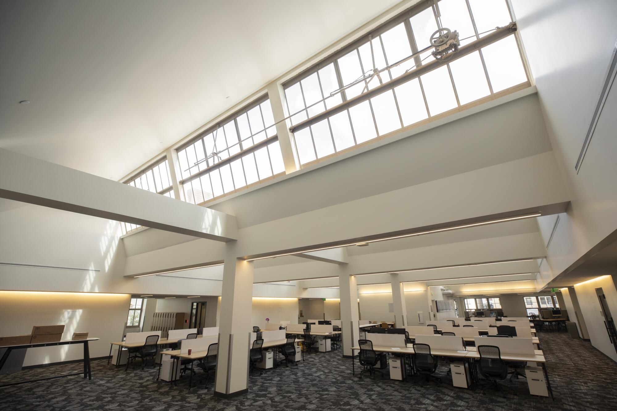 A large office space features rows of desks under sawtooth skylights that bathe the room in sunshine