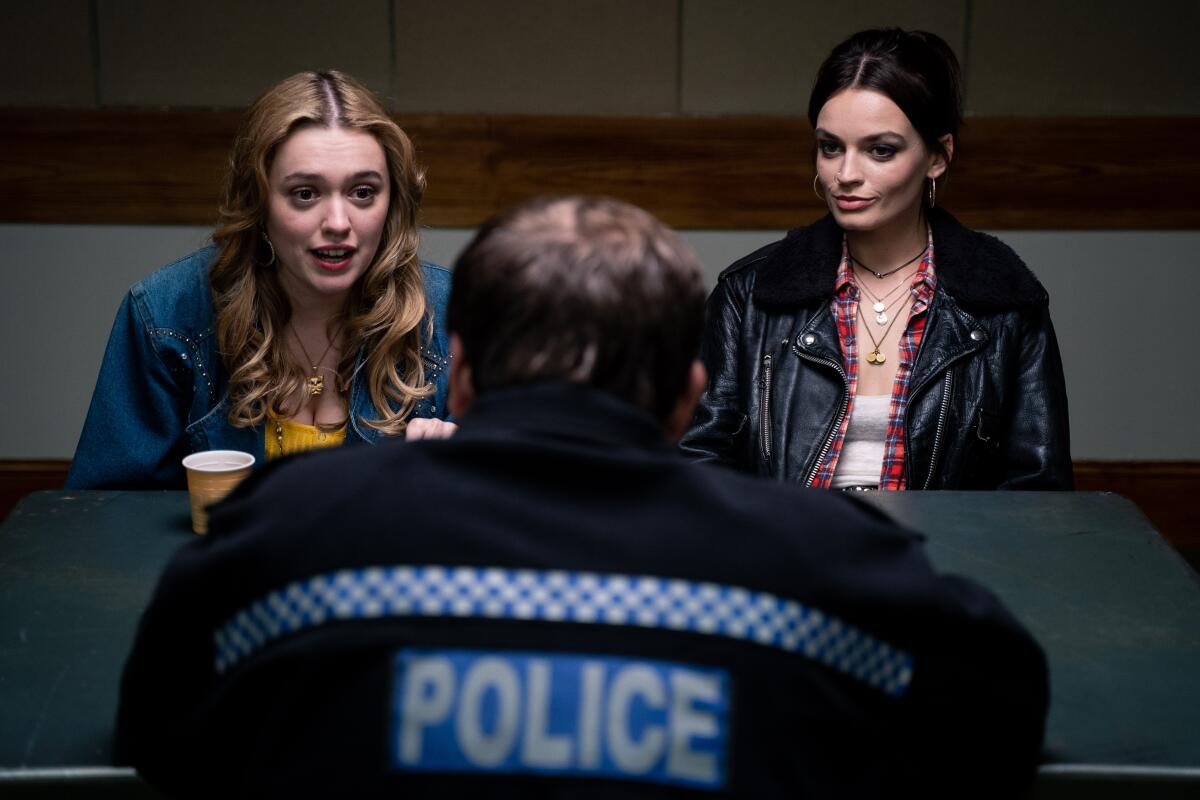 Two girls sitting at a table, speaking to a police officer.