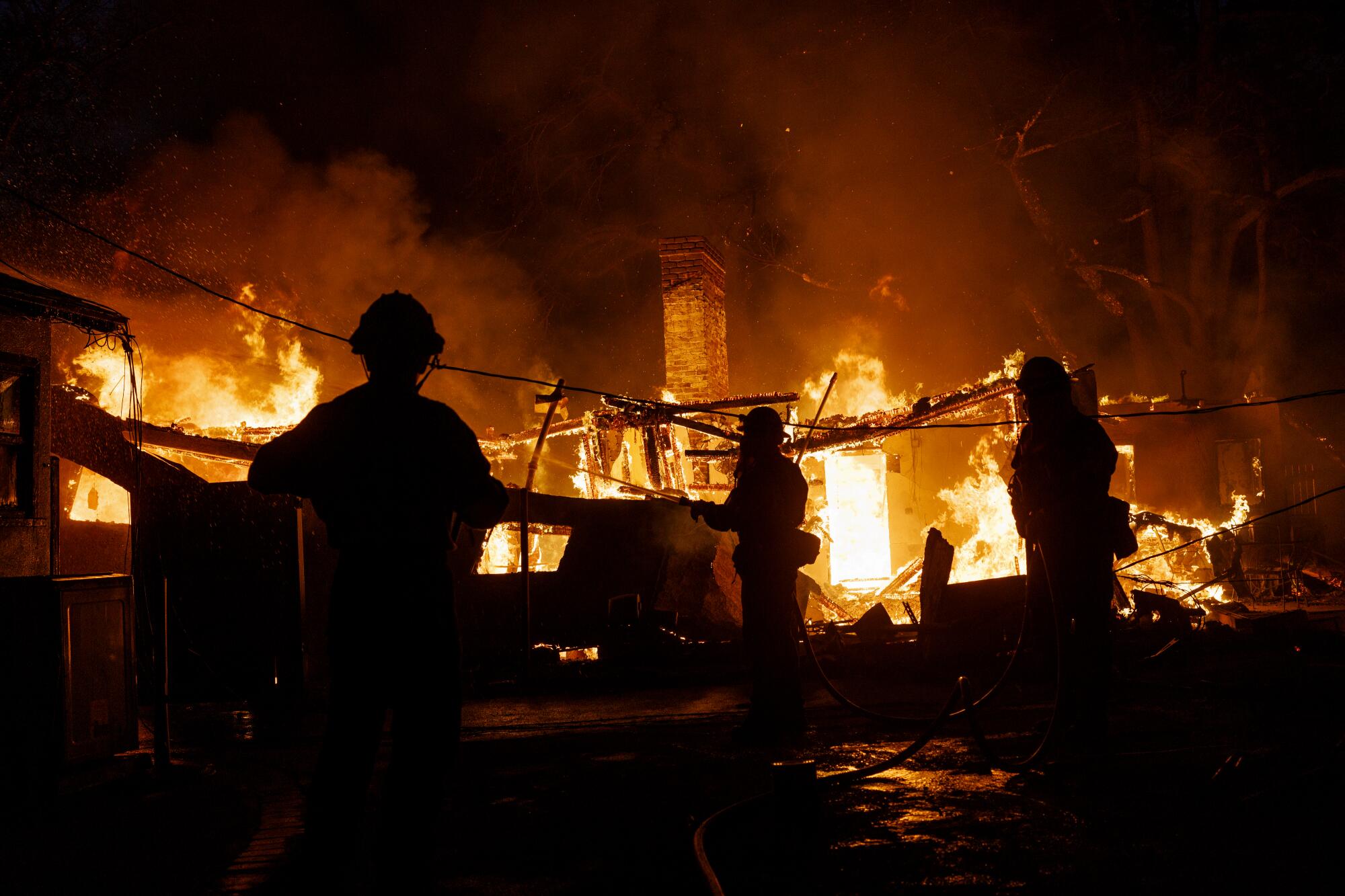 Firefighters are silhouetted against a burning home.