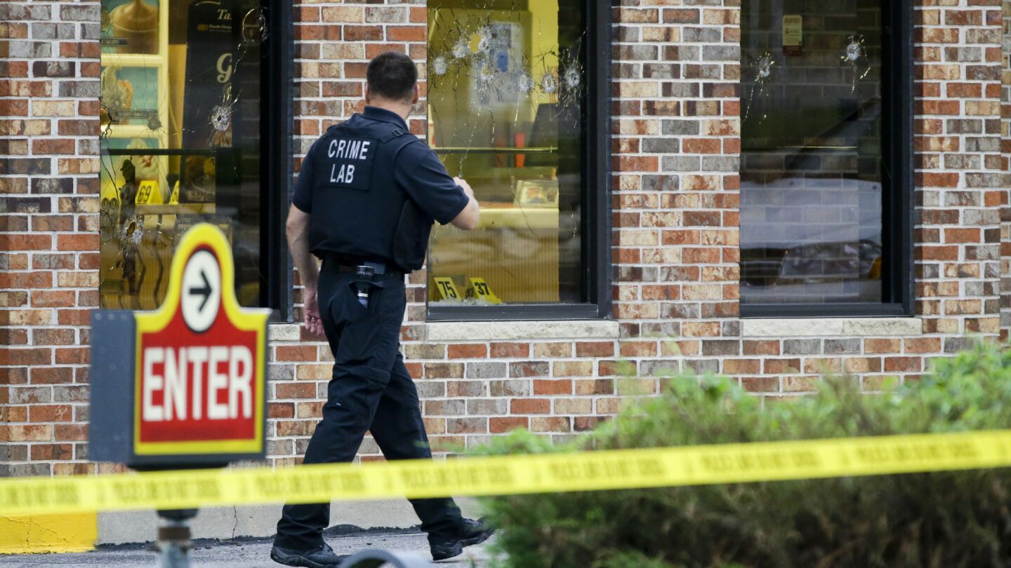 A crime lab technician walks past bullet-riddled windows at a Wendy's restaurant in Omaha on Wednesday. Police say a robber was killed by officers Tuesday night, along with a crew member of the "Cops" television show.