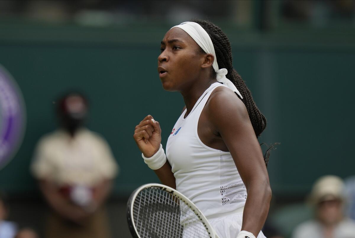 Coco Gauff, a racket in one hand, makes a fist as she crosses the tennis court.