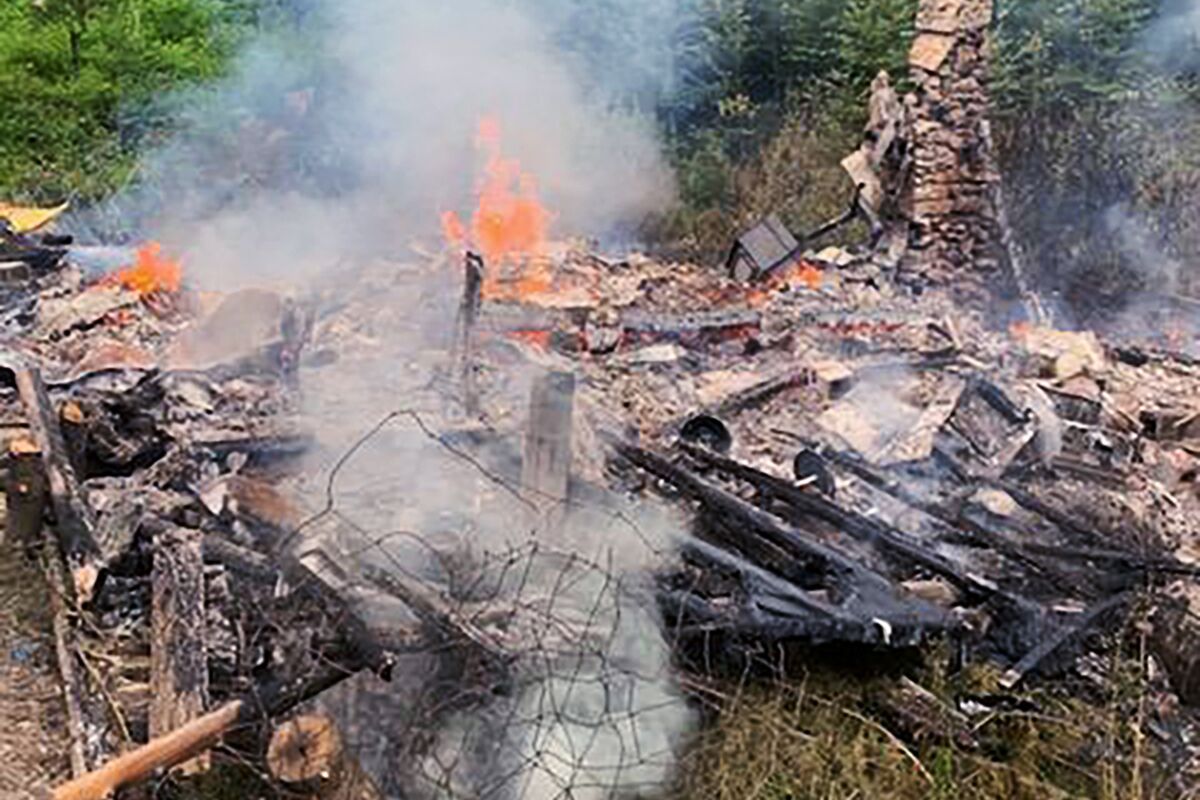 In this photo provided by the Canterbury (New Hampshire) Fire Department, smoke rises Wednesday, Aug. 4, 2021, from the burnt remains of a cabin in Canterbury, N.H., inhabited by 81-year-old David Lidstone, who for 27 years has lived in the woods of New Hampshire along the Merrimack River in the once small, solar-paneled cabin. "River Dave," as he's known by boaters and kayakers, has been jailed since July 15 after being accused of squatting for 27 years on the private property. The Canterbury fire chief said there will be an investigation into the fire. (Canterbury Fire Department via AP)