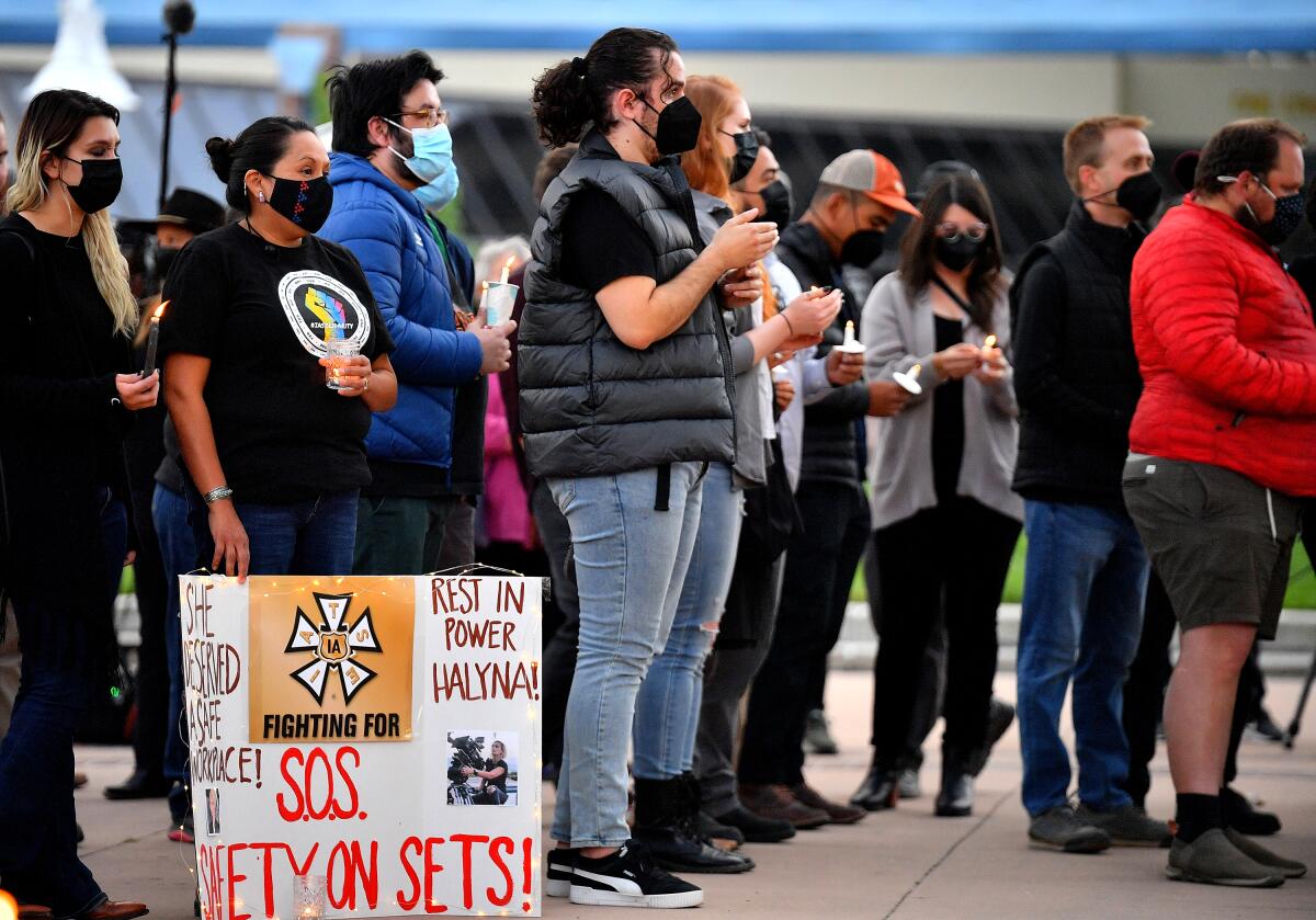 A group of people gather for a candlelight vigil. One holds a sign calling for safety on sets.