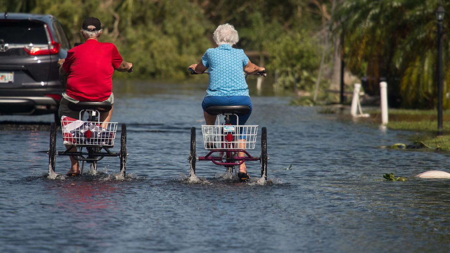 Two retirees ride tricycles through a flooded street at the Enchanted Shores manufactured home park in Naples, Florida, on September 11, 2017 after Hurricane Irma hit Florida.