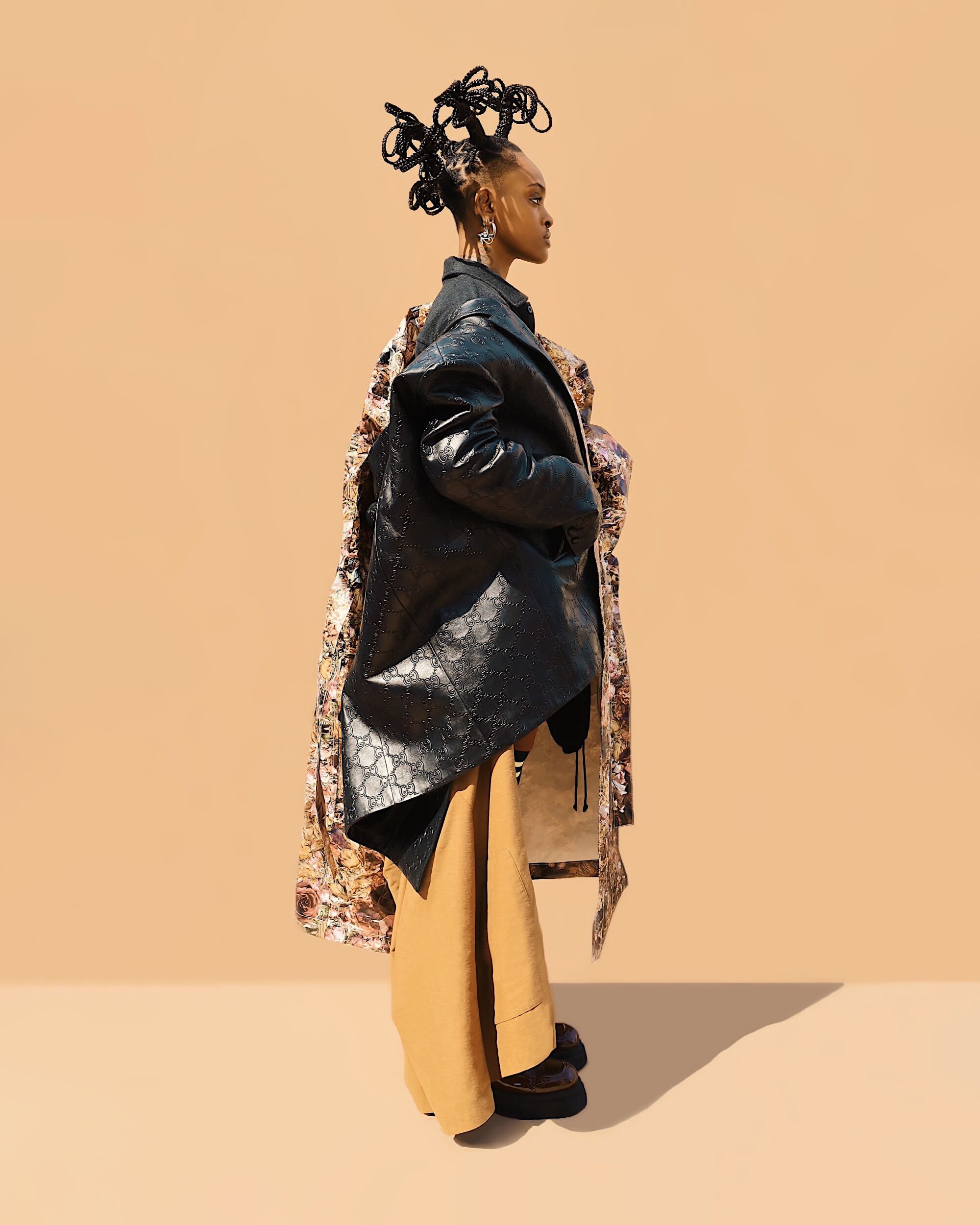 Model Lia Bass stands in front of a light brown backdrop with various high-end jackets draped sculpturally on them