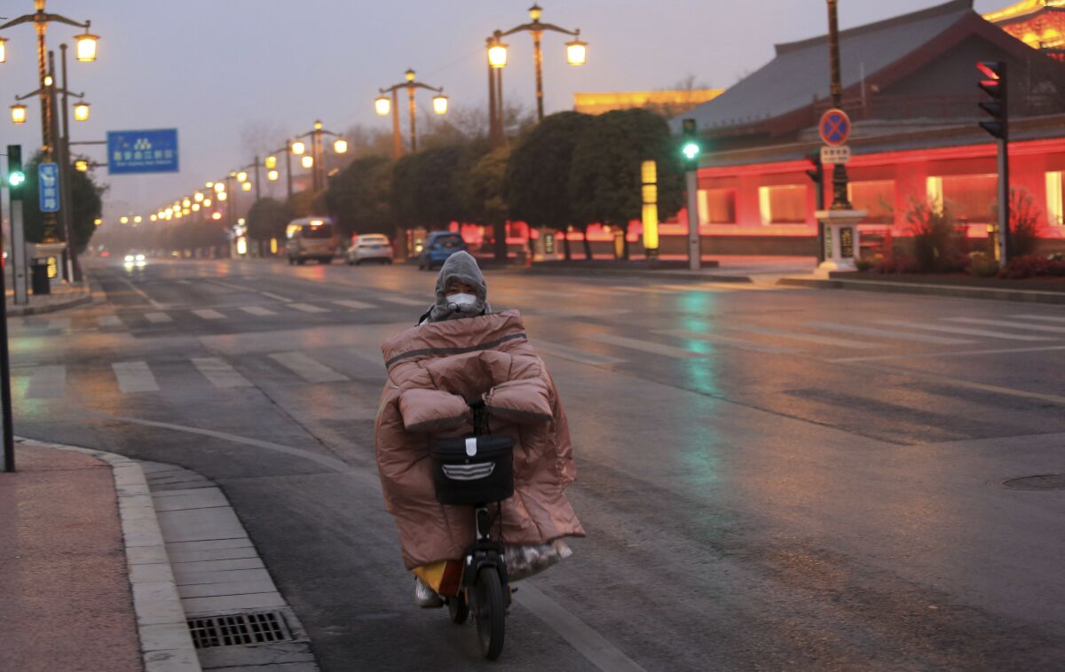 A woman wearing a face mask to protect against COVID-19 rides down a mostly empty street in Xi'an in northwestern China's Shaanxi Province, Thursday, Jan. 6, 2022. China's lockdown of big cities to fight coronavirus outbreaks is prompting concern about more disruptions to global industries after two makers of processor chips said their factories were affected. (Chinatopix via AP)