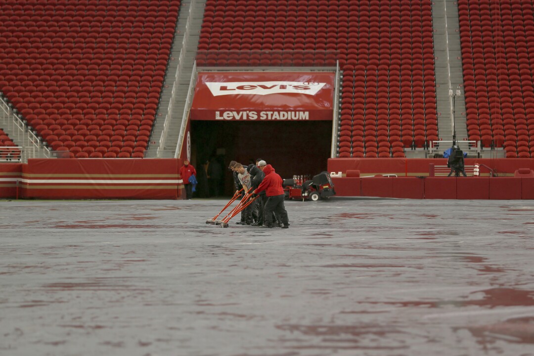 Workers push rainwater off a tarp covering the field at Levi's Stadium