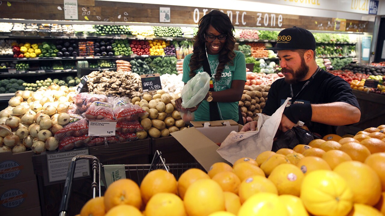 Matthew Otsuka, a team member at the Whole Foods Market in Sherman Oaks, opens a box of peaches for Instacart shopper Kara Pete as she fills the online grocery order placed by Tricia Carr.