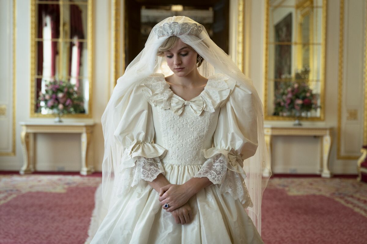 Emma Corrin as Princess Diana stands with eyes downcast and wearing an elaborate, puff-sleeved wedding dress.