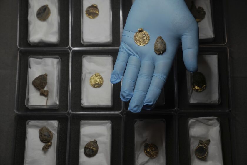 Liz Barham, curadora principal del Museo de Arqueología de Londres, muestra una gema durante una sesión de fotos, en Londres, el martes 6 de diciembre de 2022. (AP Foto/Kin Cheung)