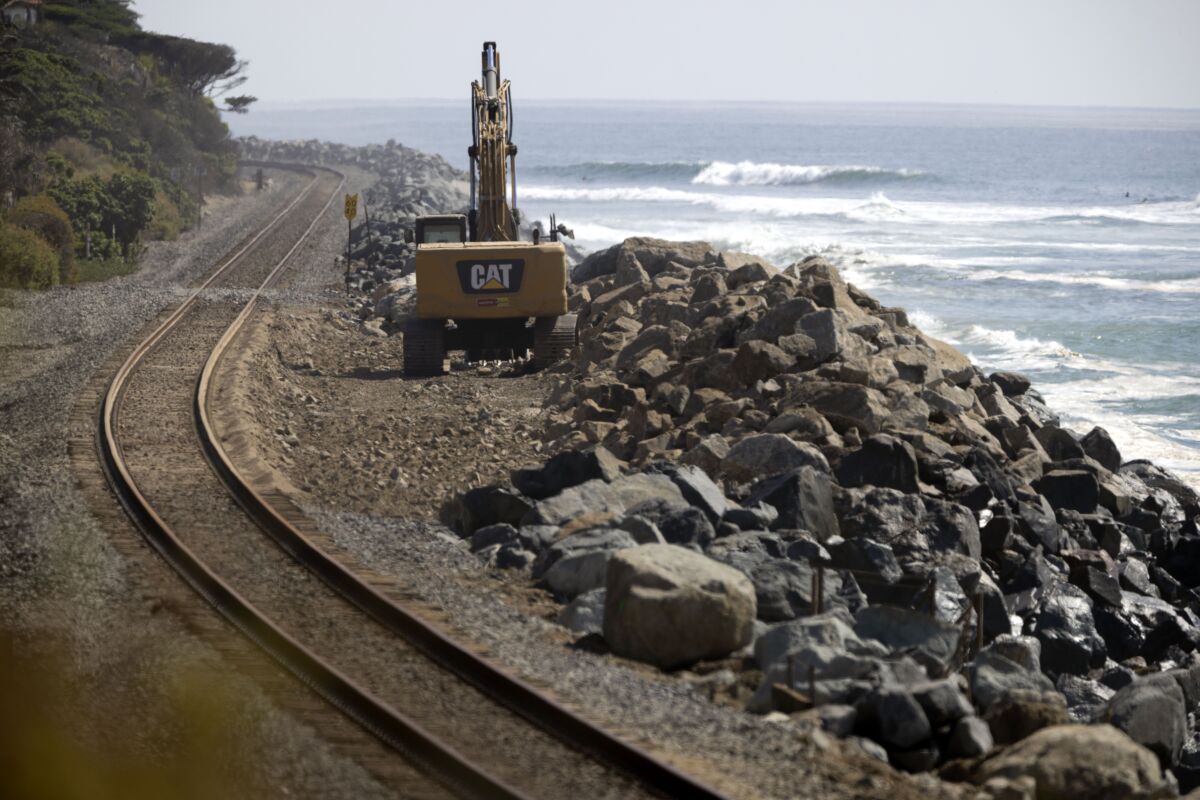 An excavator sits parked next to a section of railroad tracks