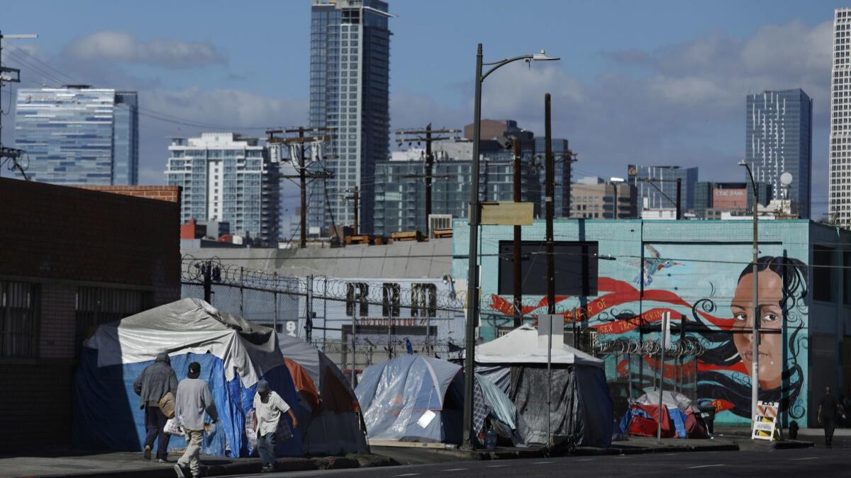People walk past a homeless encampment on 6th St., just west of Central Ave. in downtown Los Angeles on Oct. 11