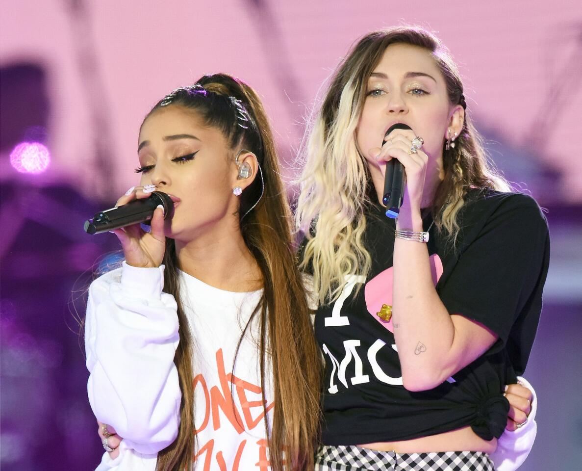 Ariana Grande, left, and Miley Cyrus perform on stage in Manchester, England.