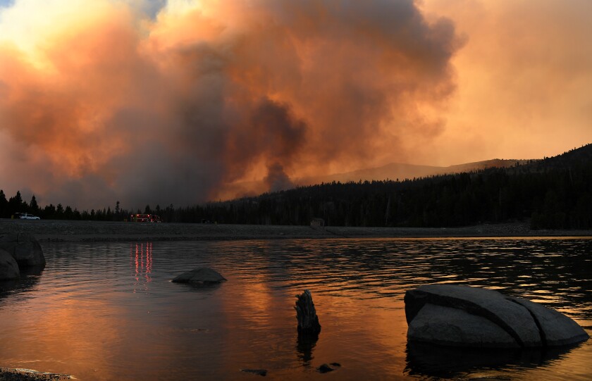Thick smoke rises behind a lake.
