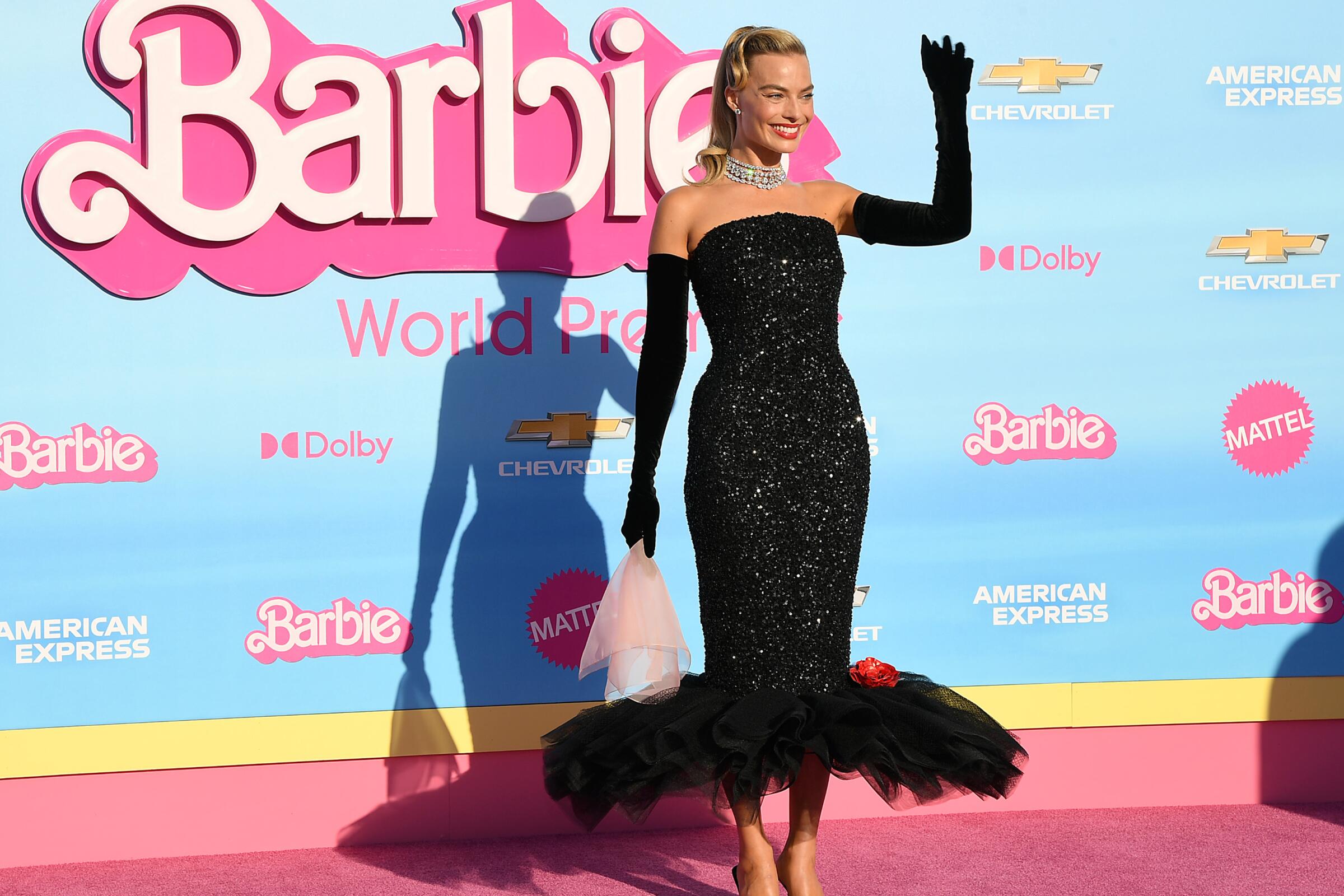 Margot Robbie waves wearing a sequined black gown on the pink 