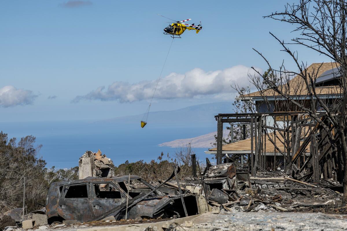 Homes lie in ashes as a helicopter continues to drop water on nearby hot spots