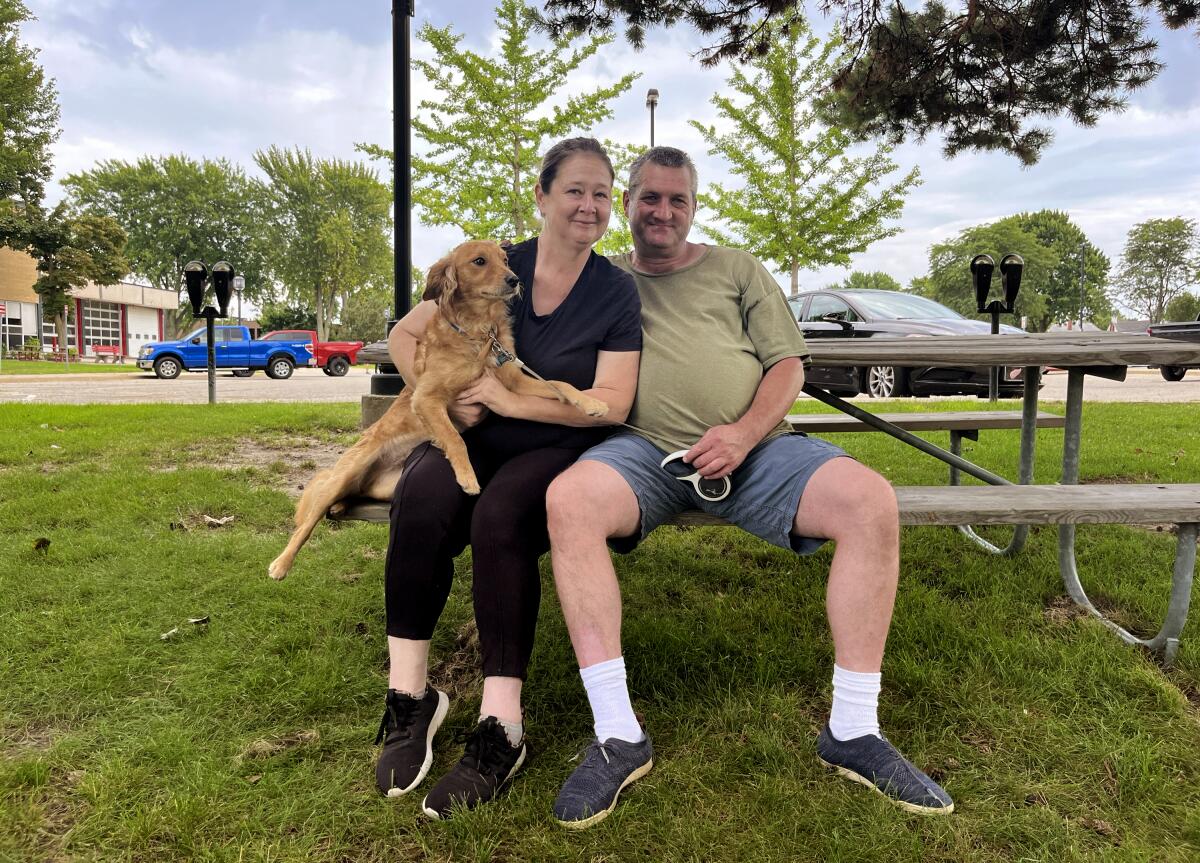 Mickey Kraft and Kristy Kitchen sit sit on a park bench with a dog