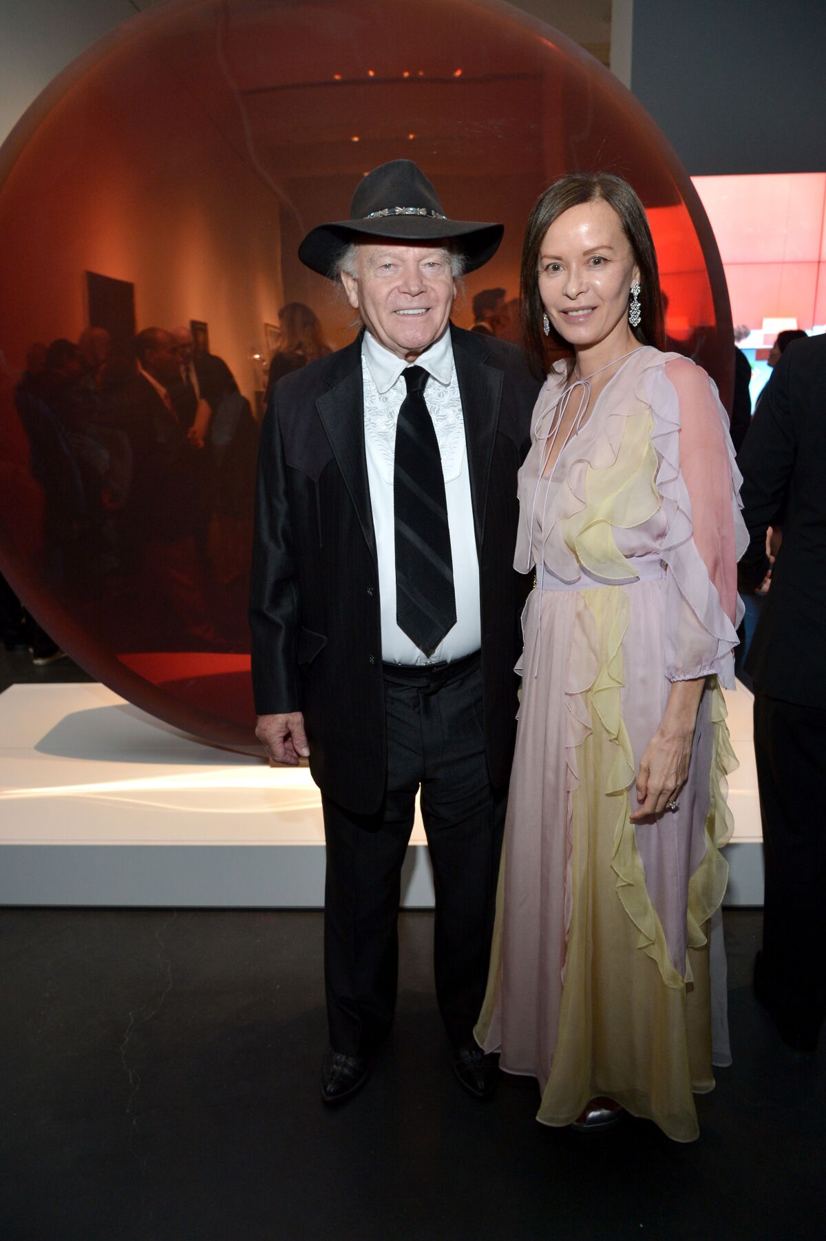 A man in a suit and cowboy hat stands with a woman in a pastel gown with frills.