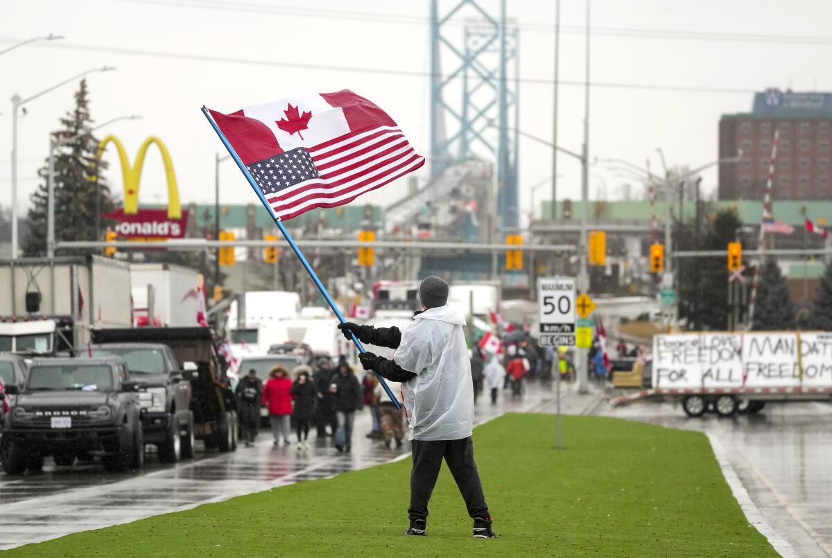 A man waves a Canadian and a U.S. flag on one pole near a line of trucks.
