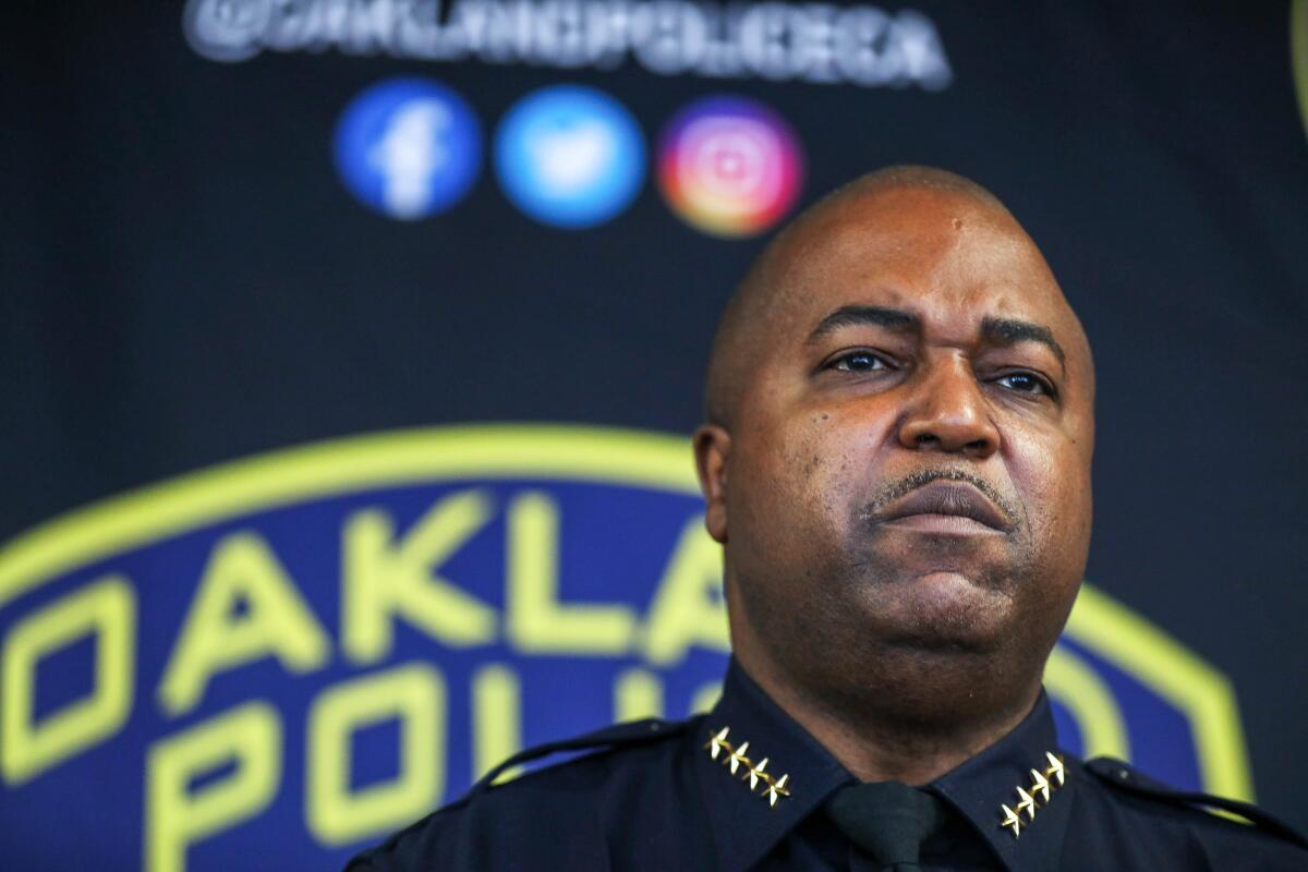 A police chief in uniform stands in front of the Oakland Police Department logo