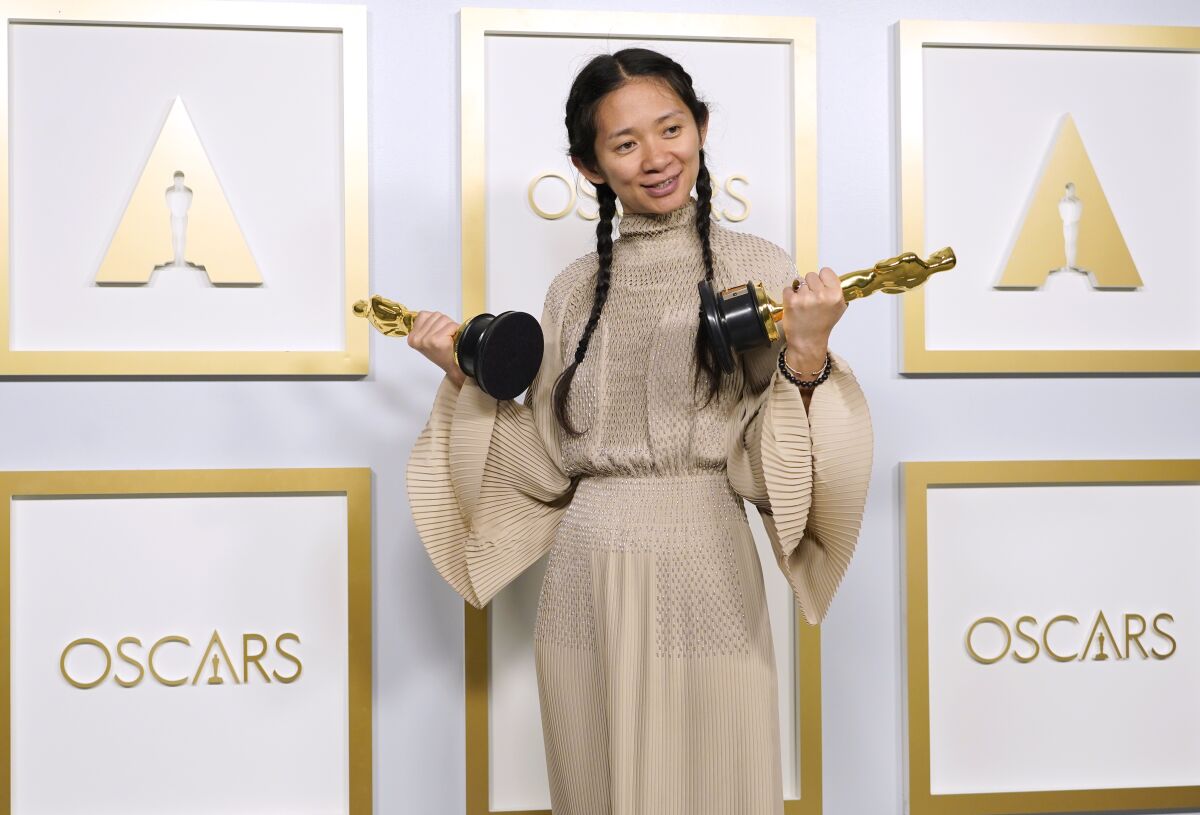 a woman holding an Oscars trophy in each hand