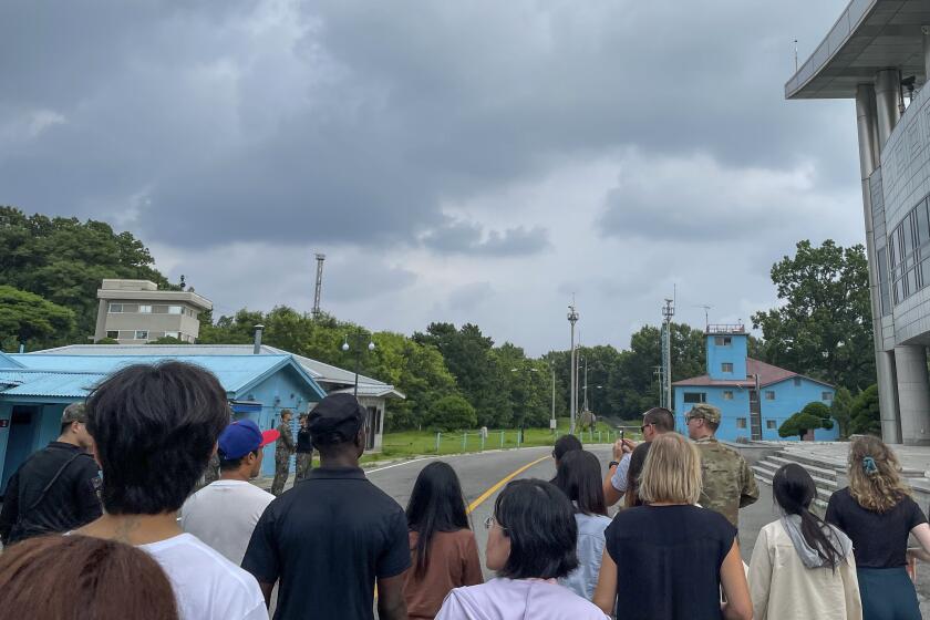 UPDATED CAPTION: A group of tourists stand near a border station at Panmunjom in the Demilitarized Zone in Paju, South Korea, Tuesday, July 18, 2023. Not long after this photo was taken, Travis King, a U.S. soldier, pictured with dark blue shirt and dark cap, fourth left, bolted across the border and became the first known American detained in the North in nearly five years. (AP Photo/Sarah Jane Leslie)