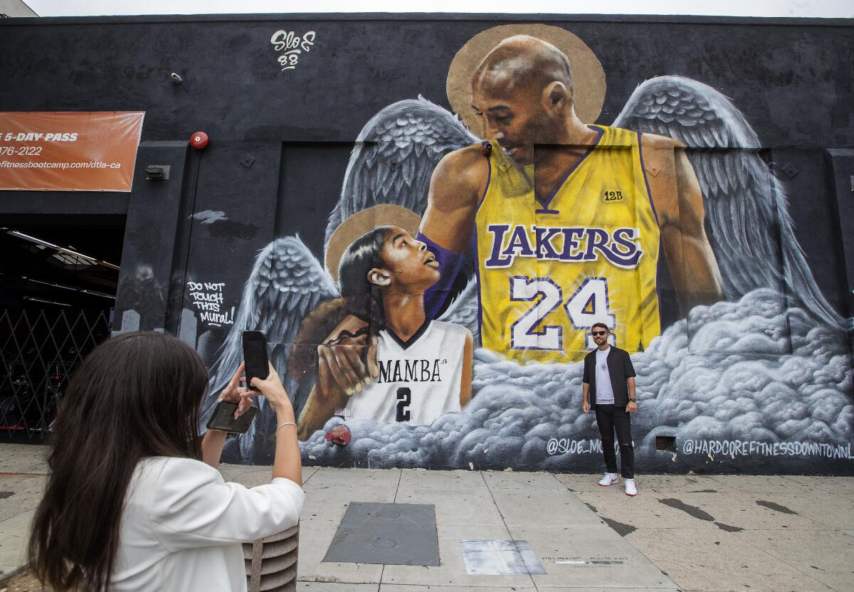 A man poses in front of a mural of Kobe and Gianna Bryant.