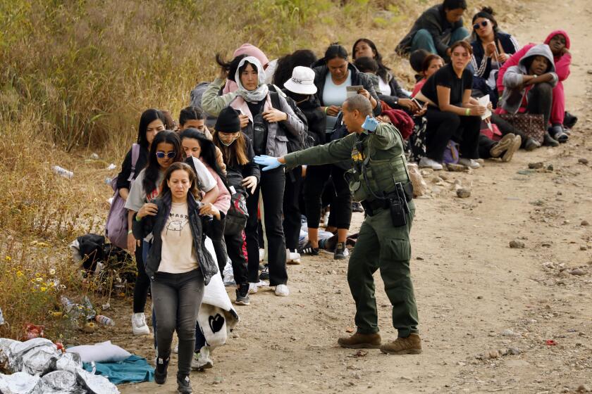U.S. border, United States-May 11, 2023-With less than 24 hours until Title 42 expires, U.S. border patrol agents lead a group of women to vehicles headed to processing. Migrants hoping to cross into the United States from Tijuana, Mexico on May 11, 2023 are being processed more quickly as the deadline approaches. Some migrants have been waiting a week in an area south of the second border wall in anticipation of a change in immigration policy, Title 42, which may allow them to apply for asylum. U.S. border patrol agents give out one bottle of water and one granola bar to each person. There are approximately 500 people in this one camp. (Carolyn Cole / Los Angeles Times)