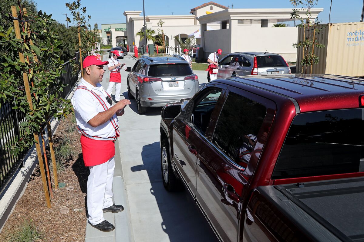Employees take orders as customers line up for the drive-through during opening day at the new In-N-Out Burger.