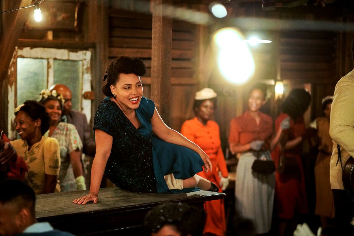 A smiling woman sits on a countertop as other people stand in the room around her.