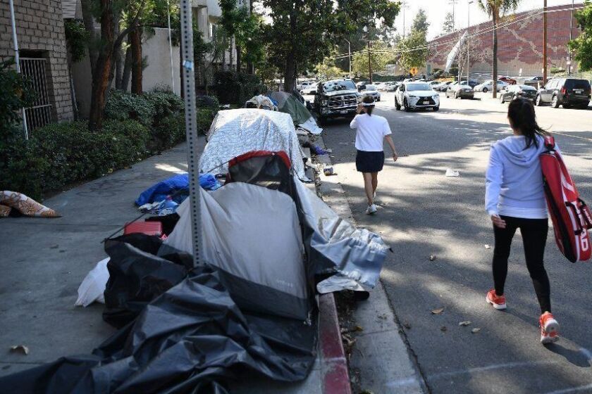 LOS ANGELES, CALIFORNIA MAY 16, 2019-Pedestrians walk along the street instead of the sidewalk where homeless people set up tents outside the Villa Adobe apartment building in Koreatown. (Wally Skalij/Los Angeles Times)