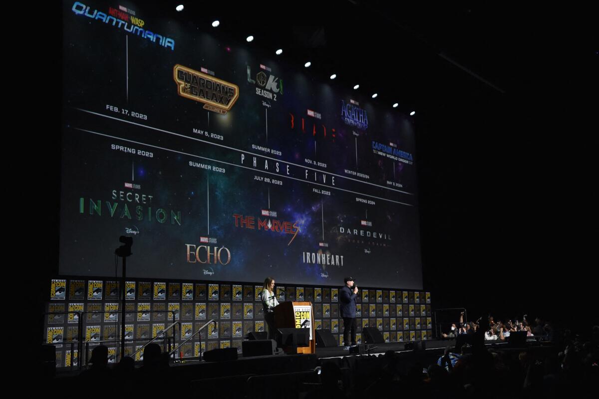 President of Marvel Studios Kevin Feige speaks on a stage in front of a screen with show titles on it.