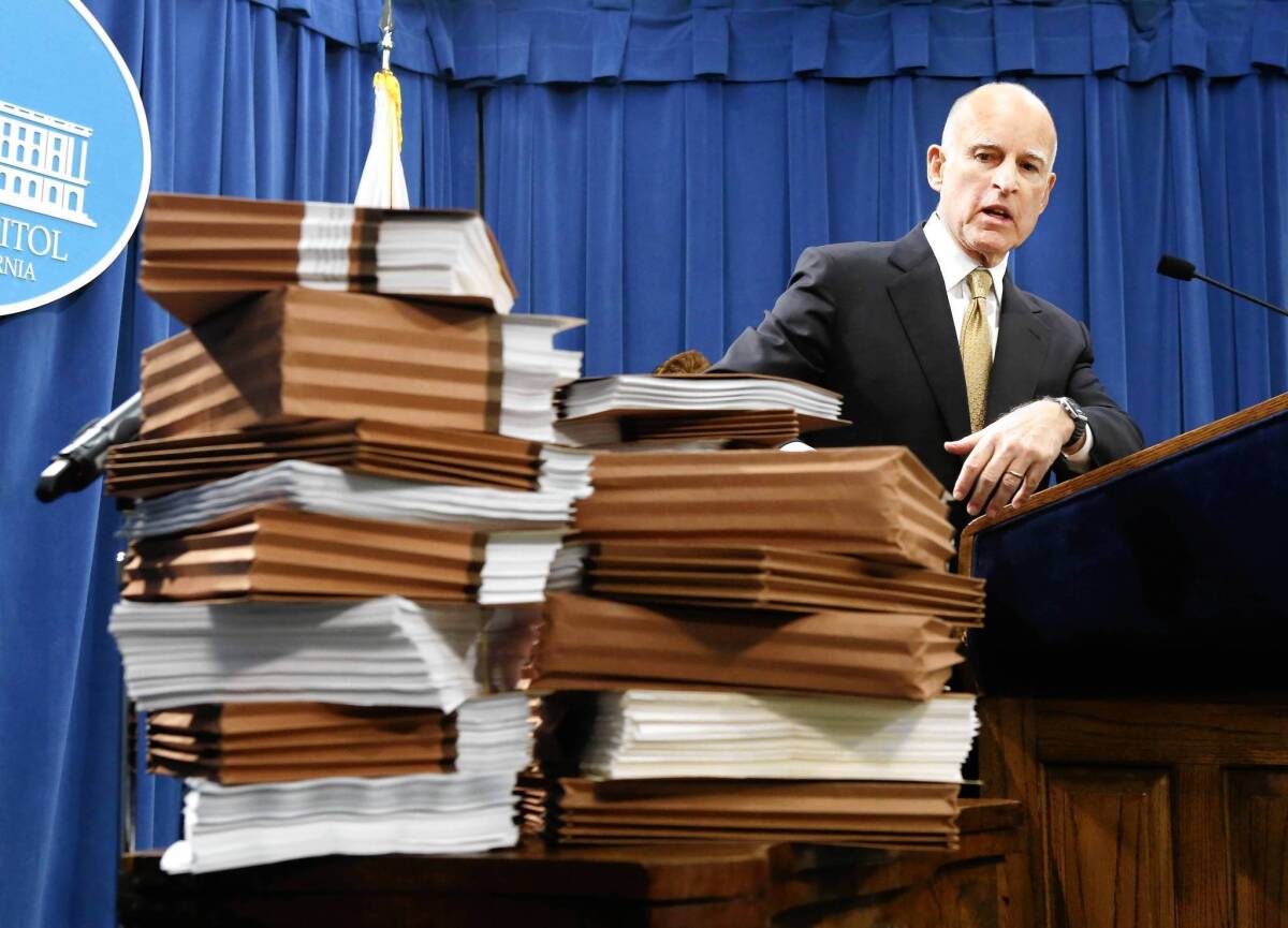 Gov. Jerry Brown gestures to a stack of reports on California prisons as he discuss his call for federal judges to return control of prisons to the state during a news conference in Sacramento on Tuesday.