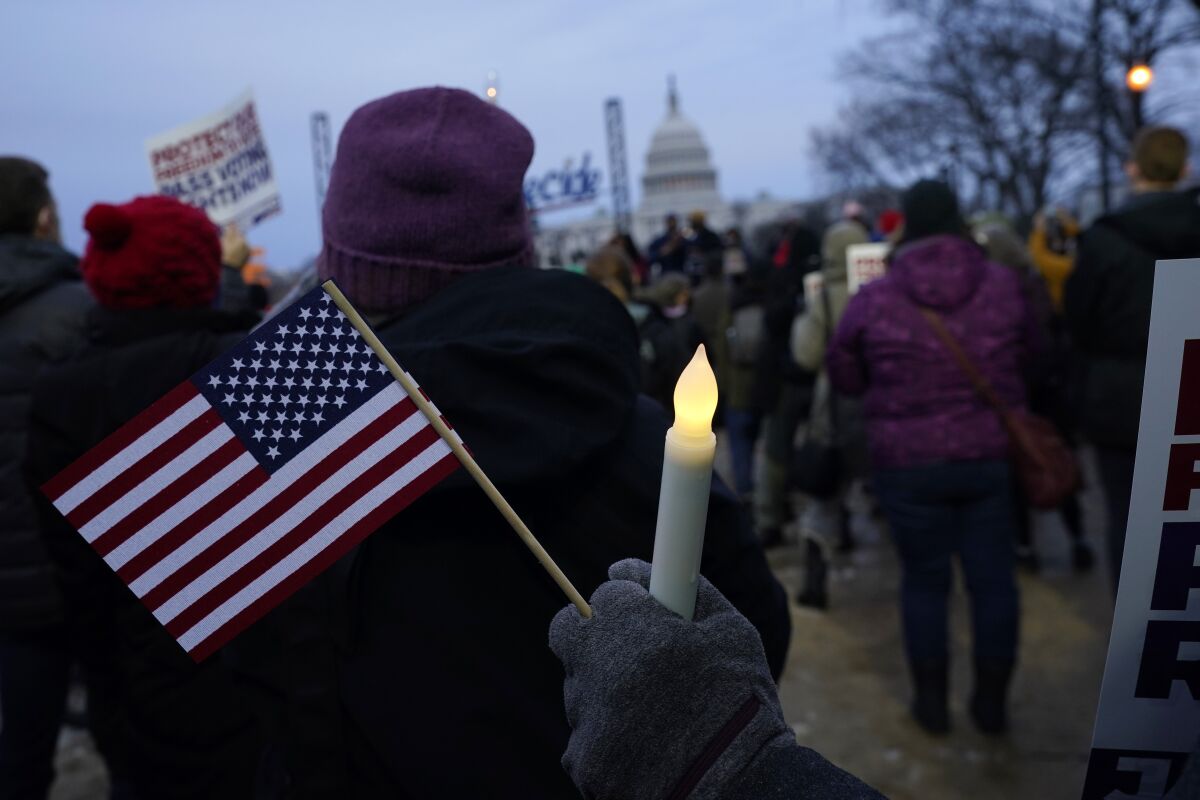 With the U.S. Capitol building in the background, a person holds an American flag and a flameless candle during a vigil Thursday, Jan. 6, 2022, in Washington, on the one year anniversary of the attack on the U.S. Capitol. (AP Photo/Julio Cortez)