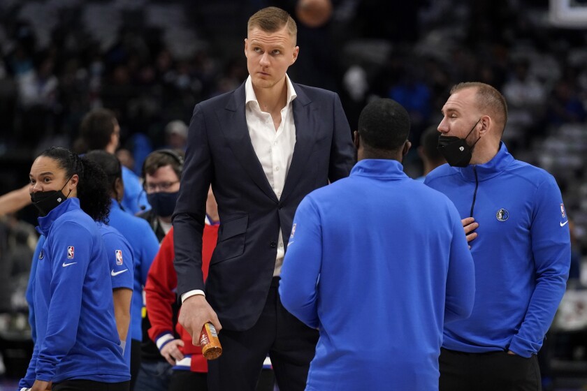 Dallas Mavericks' Kristaps Porzingis, center, stands on the court talking with staff before the first half of a NBA basketball game against the Oklahoma City Thunder in Dallas, Wednesday, Feb. 2, 2022. Porzingis did not play in the game. (AP Photo/Tony Gutierrez)