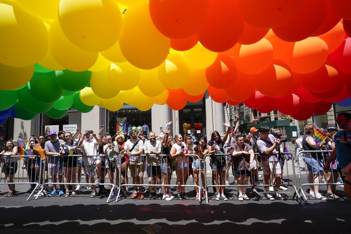 Spectators watch behind barricades as revelers march down a street with multicolored balloons during a parade