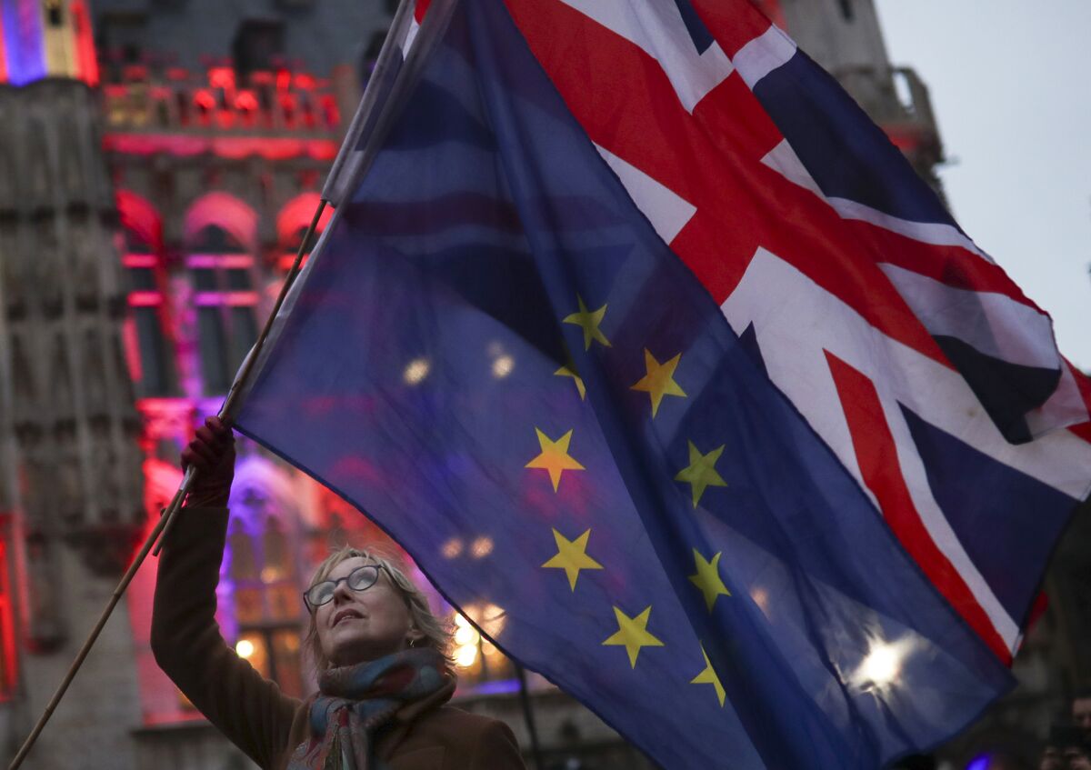 FILE - In this file photo dated Thursday, Jan. 30, 2020, a woman holds up the British Union and the European Union flags together during an event in Brussels, Belgium. The number of Britons moving to live in European Union countries has soared since the Brexit vote in 2016, a U.K.-German study has revealed Tuesday Aug. 4, 2020. (AP Photo/Francisco Seco, FILE)