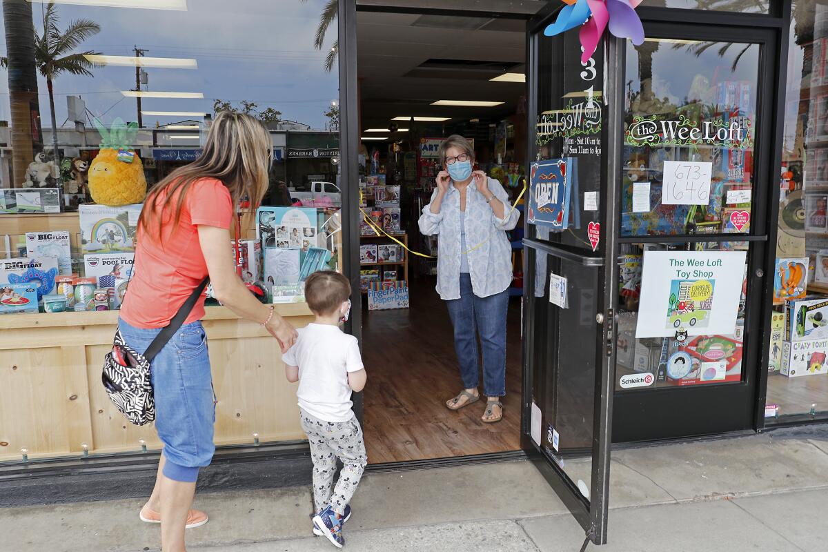 Owner Erin Kelly, right, adjusts her face mask as she welcomes longtime customer Eva Stellar, left, with her son Jake, 4, for curbside pickup on May 8 at the Wee Loft, an independent toy store in Corona del Mar.