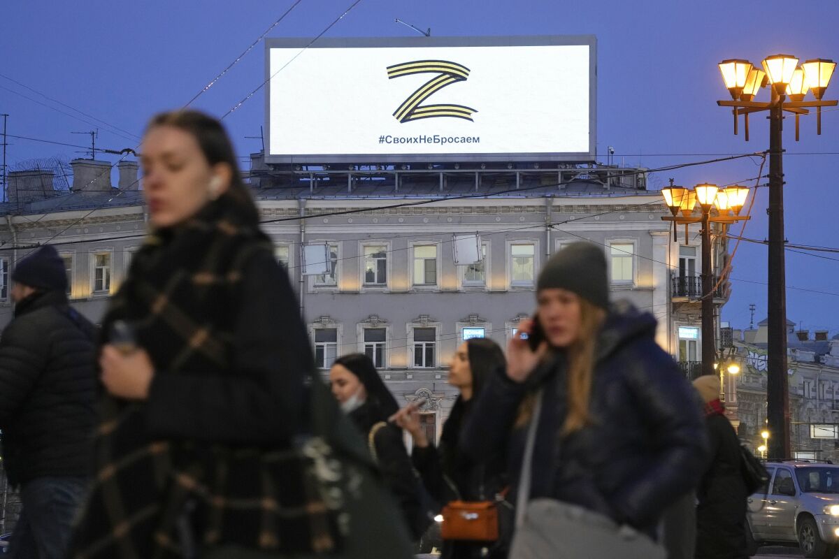 People walk past the letter Z, which has become a symbol of the Russian military, and a hashtag reading "We don't abandon our own" on an advertisement screen in St. Petersburg, Russia, Wednesday, March 9, 2022. (AP Photo)