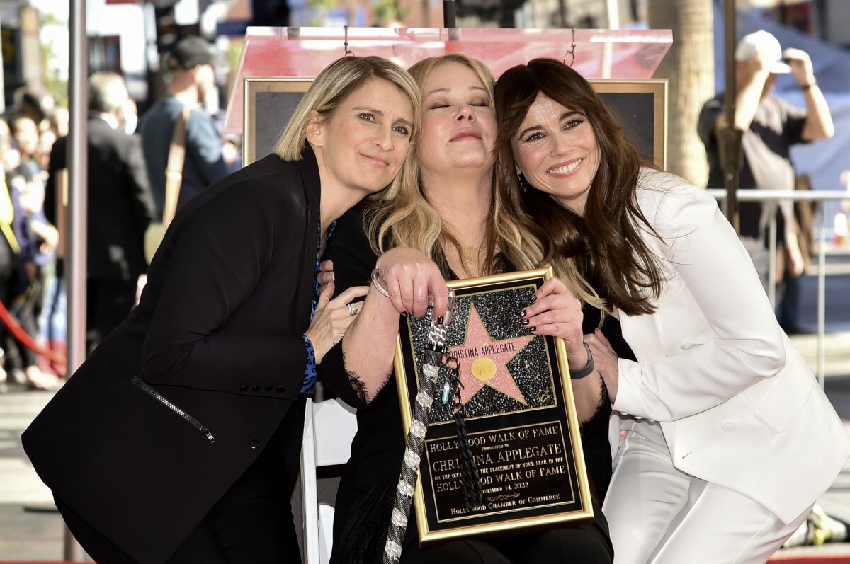 Three women pose cheek-to-cheek holding a plaque