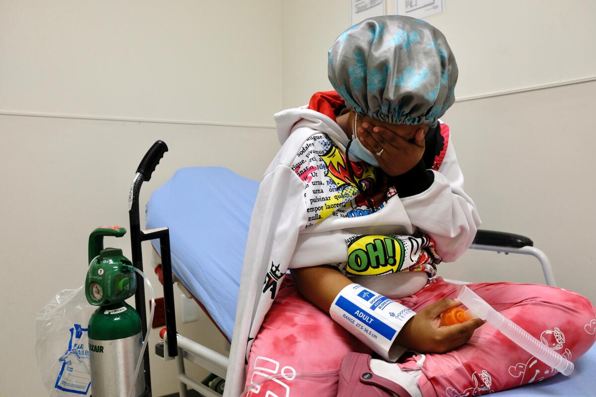 A patient on a hospital cot covers her eyes.